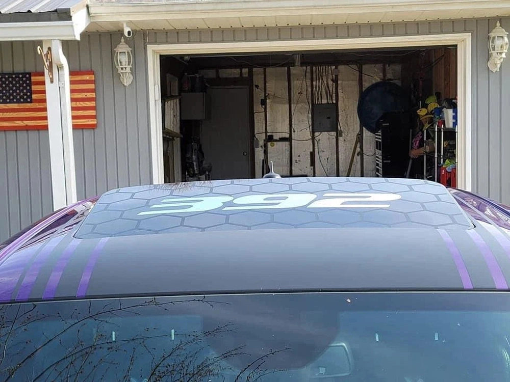 Purple Dodge Challenger with T/A logo sunroof decal parked in front of garage, showcasing custom vinyl design for vehicle customization. American flag visible in background.