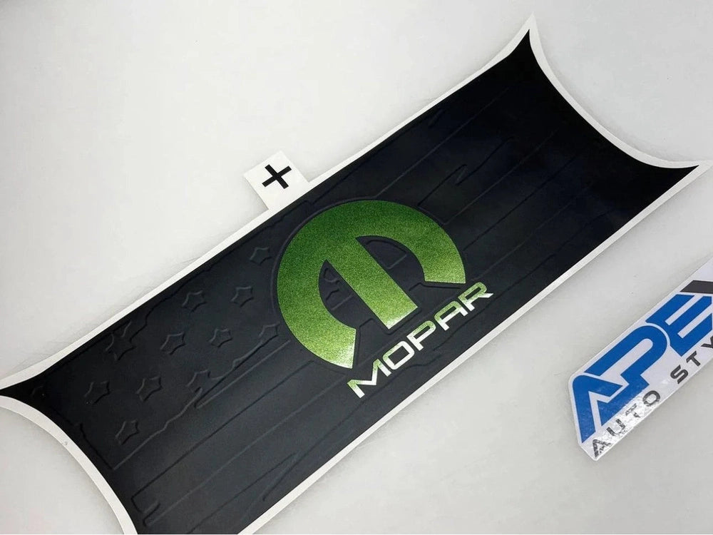 Challenger taillight divider decal with green MOPAR logo on black background, featuring embossed star pattern and curved edges. Product packaging visible in corner.