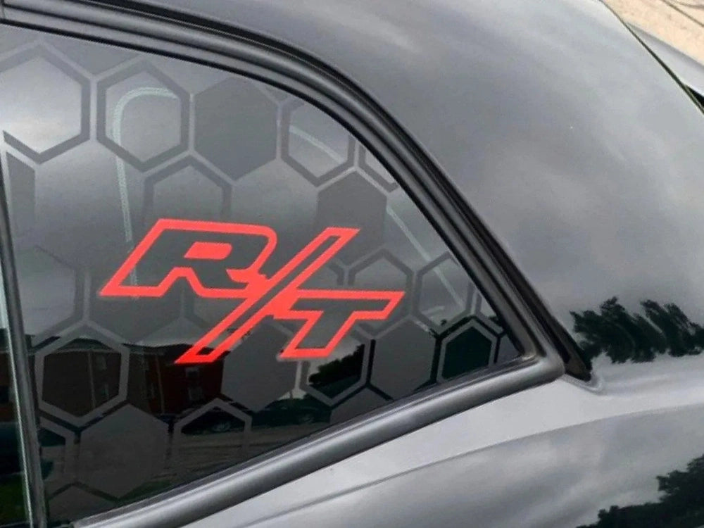 Close-up of a Dodge Challenger quarter window featuring a red R/T logo decal against a black hexagonal pattern background, showcasing the custom vinyl decal product for Challenger vehicles.