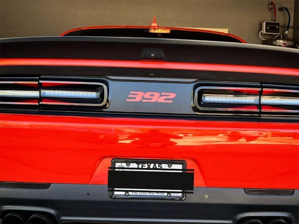 Close-up rear view of a red Dodge Challenger, showcasing the taillight area with a black divider strip featuring a red 392 logo, highlighting the customizable taillight divider decal product for 2015+ models.