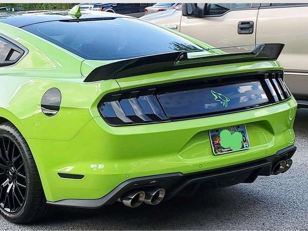 Rear view of a bright green Ford Mustang S550 model, showcasing its distinctive taillights, spoiler, and dual exhaust pipes. The car's sleek and sporty design is emphasized by its vibrant color and aggressive styling elements.