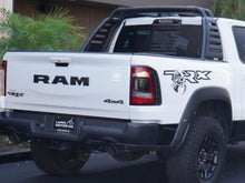 Load image into Gallery viewer, White RAM TRX pickup truck with custom bedside decal featuring TRX logo and stylized dinosaur graphic, parked in front of green foliage
