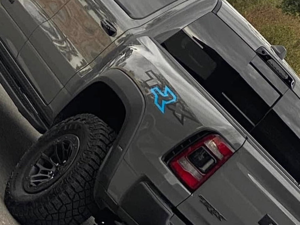 RAM TRX truck bedside decal featuring TRX logo with customized blue R, displayed on silver vehicle body above off-road tire and near taillight, showcasing product application and design