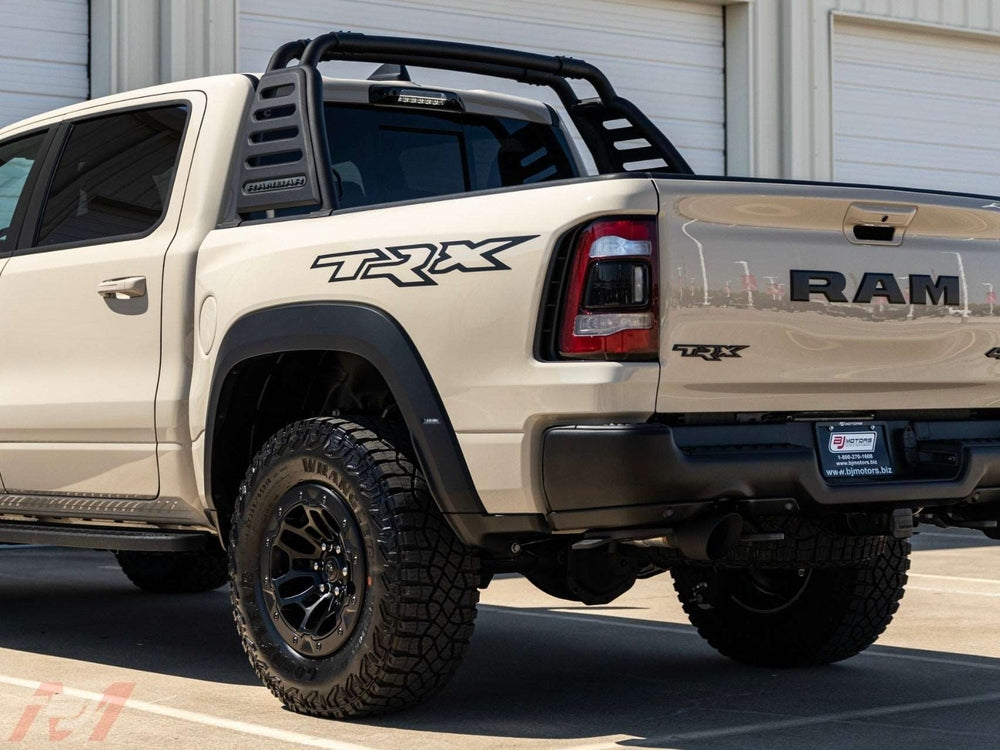 RAM TRX pickup truck with prominent TRX bedside decal, showcasing the product in its intended application on a beige vehicle with off-road tires and a black roll bar, parked in front of a garage door