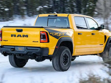 Load image into Gallery viewer, Yellow RAM TRX pickup truck driving on snowy road, showcasing bedside decal with TRX logo. Rugged off-road tires and distinctive RAM tailgate visible. Winter forest background highlights the truck&#39;s adventurous capabilities.