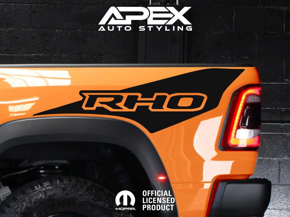 Close-up of orange RAM truck bedside featuring RHO decal, showcasing sleek design and vibrant color contrast against black background with Apex Auto Styling logo visible