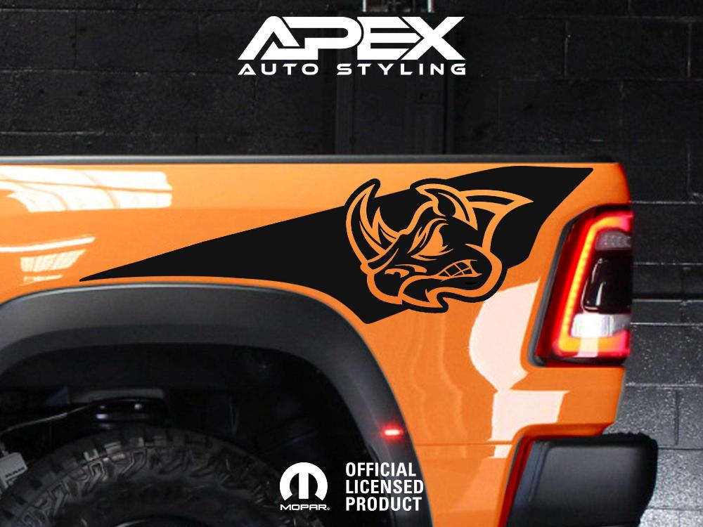 Orange RAM truck bedside with black RHO rhino head logo decal, showcasing Apex Auto Styling product on display against dark background