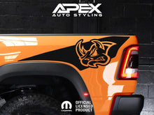 Load image into Gallery viewer, Orange RAM truck bedside with black RHO rhino head logo decal, showcasing Apex Auto Styling product on display against dark background