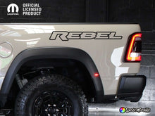 Load image into Gallery viewer, RAM Rebel truck side view showing bedside decal with &#39;REBEL&#39; text, taillight, and large off-road tire, highlighting the product&#39;s application and style on a light-colored vehicle against a dark background