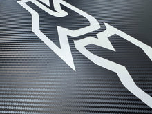 Load image into Gallery viewer, Close-up of RAM TRX hood decal with white logo cutout on carbon fiber texture background, showcasing the premium vinyl material and OEM-style design for truck customization