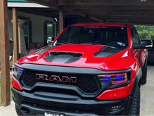 Load image into Gallery viewer, Red RAM truck with TRX logo windshield banner decal, showcasing custom styling and rugged design features including aggressive grille, hood scoop, and off-road tires