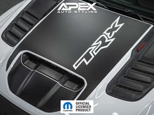 Load image into Gallery viewer, Black RAM TRX hood decal with TRX logo cutout installed on a vehicle hood, showcasing OEM-style design with contrasting white logo against dark background. Apex Auto Styling branding visible in corner.