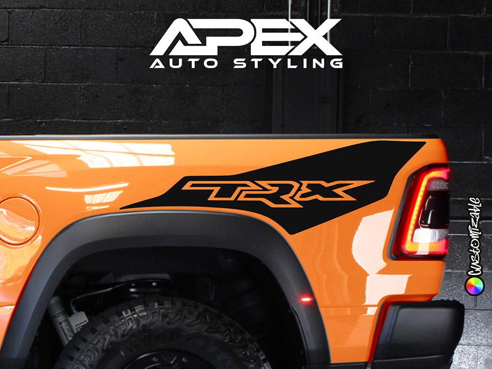 Close-up of orange RAM TRX truck bedside featuring black Ignition Style decal, showcasing custom vinyl design against vibrant paint. Apex Auto Styling logo visible in background on dark wall.