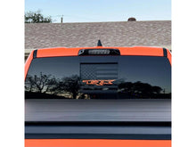 Load image into Gallery viewer, RAM truck rear window with custom TRX logo decal and American flag design, showcasing precision-cut vinyl application for 2009+ models. Orange TRX logo contrasts against black matte background, demonstrating product customization options.