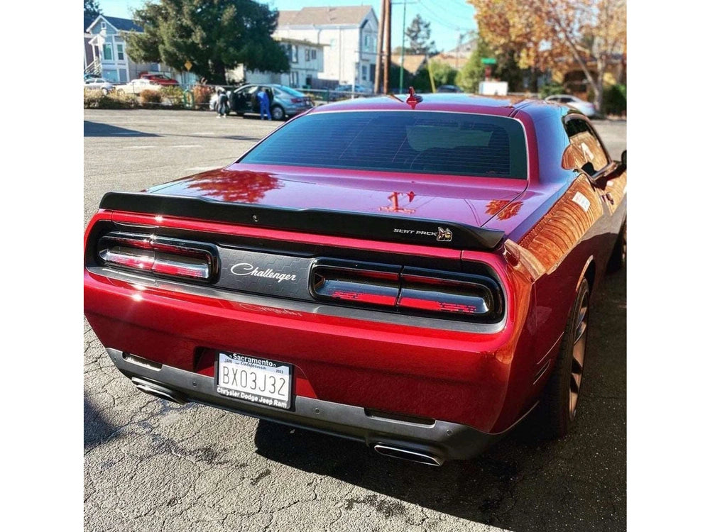 Rear view of a red Dodge Challenger parked on a street, showcasing its distinctive taillights and sleek design. The car's reflective surface highlights its muscular contours and sporty appearance.