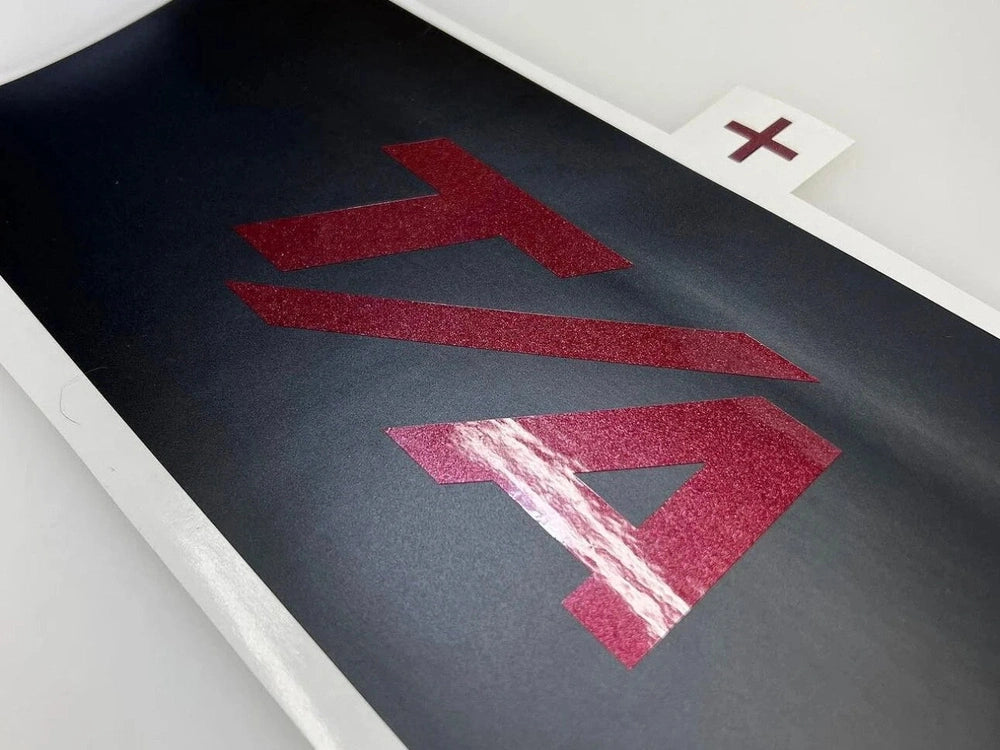 Customizable Challenger taillight divider decal featuring red T/A logo on black background. Close-up view showcasing the textured, glittery finish of the logo against smooth surface. Product sample demonstrating high-quality vinyl application and precision cut design for Dodge Challenger models.