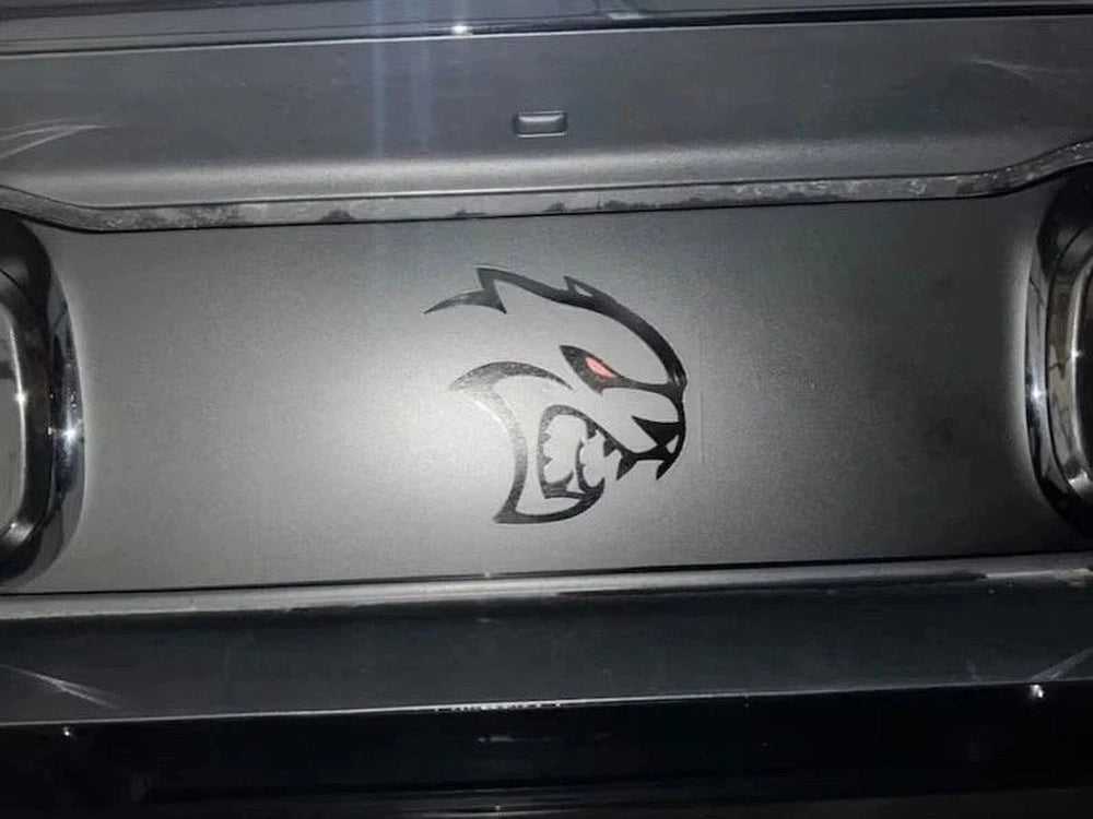 Dodge Challenger taillight divider with Hellcat Redeye logo decal applied, featuring a stylized cat head with glowing red eye between taillights on silver-gray surface