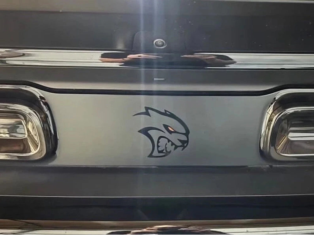 Dodge Challenger taillight divider with Hellcat Redeye logo decal applied, showcasing custom matte black design with embossed pattern and red-eyed cat emblem between taillights