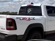 Load image into Gallery viewer, White RAM pickup truck with TRX logo on side and dinosaur decal on rear sliding window, driving on road under cloudy sky