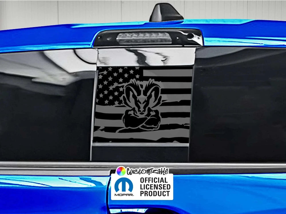 RAM truck rear sliding window with black American flag decal featuring RAM logo. Blue exterior visible. Official licensed product sticker shown.