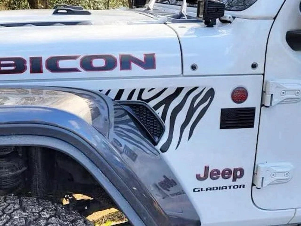 White Jeep Gladiator Rubicon with zebra stripe fender vent decals, showcasing custom Wrangler accessory for unique styling, parked outdoors on gravel road with trees visible in background