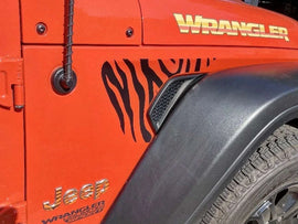 Orange Jeep Wrangler fender with zebra stripe decal, showcasing custom fender vent design for Wrangler and Gladiator models. Close-up view highlighting the contrast between vibrant vehicle color and black striped pattern.