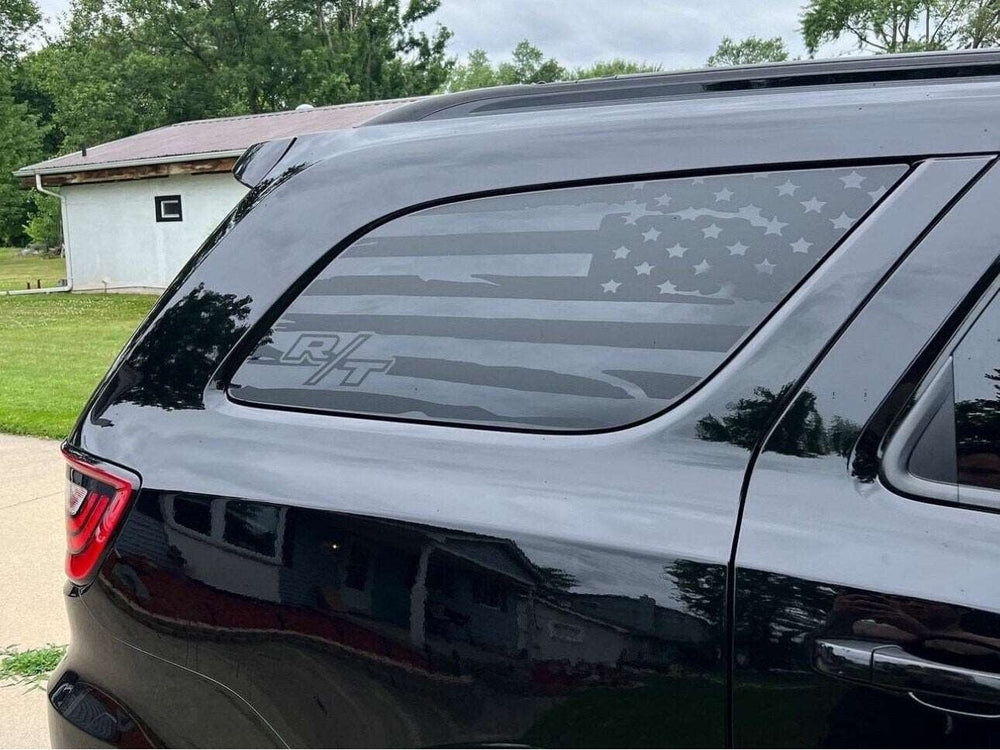 Dodge Durango quarter window decal featuring R/T logo and American flag design in matte black, applied to rear side window of dark-colored SUV parked in grassy area with trees in background
