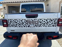 Load image into Gallery viewer, Jeep Gladiator tailgate with cheetah print decal, showcasing black spotted pattern on white background. Jeep logo visible in center. Rear view of truck parked in driveway.