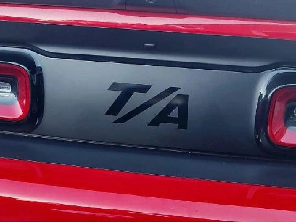 Close-up of a Dodge Challenger taillight divider with T/A logo decal applied, showcasing customized appearance between red taillights on a black and red vehicle exterior
