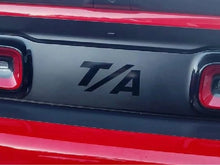 Load image into Gallery viewer, Close-up of a Dodge Challenger taillight divider with T/A logo decal applied, showcasing customized appearance between red taillights on a black and red vehicle exterior