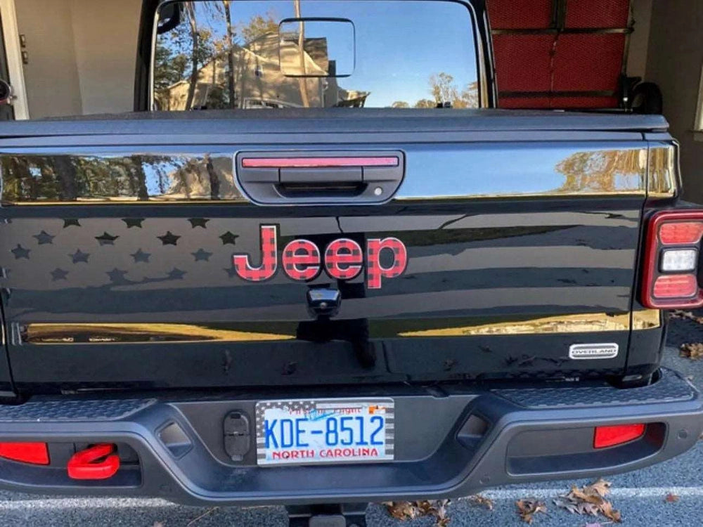 Jeep Gladiator tailgate with American flag decal, featuring red Jeep logo and black background with stars and stripes pattern, parked in driveway showing North Carolina license plate