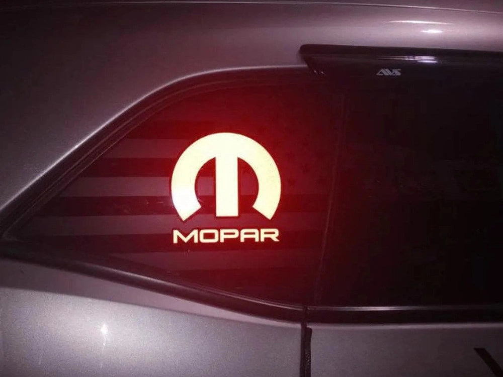 Illuminated MOPAR logo decal on Dodge Challenger quarter window, glowing red against dark background, showcasing custom vinyl application for sporty aesthetic