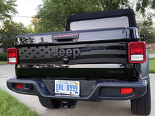 Load image into Gallery viewer, Jeep Gladiator tailgate with American flag decal, showcasing patriotic design on black surface. Tailgate features Jeep logo and license plate visible. Rear view of truck parked on residential street with trees in background.