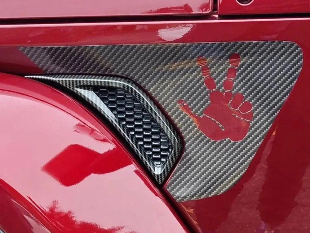 Close-up of a red Jeep Wrangler or Gladiator fender vent with a carbon fiber look decal featuring a red peace sign hand symbol, showcasing the custom Fender Vent Decal product for Jeep vehicles