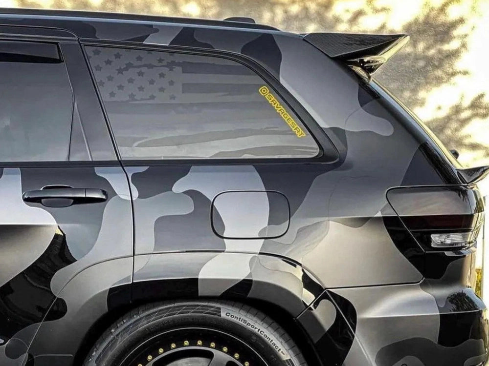 Jeep Grand Cherokee with American flag decal on quarter window, showcasing custom patriotic design for 2011-2021 models. Gray vehicle exterior with black trim, highlighting the matte black vinyl application on rear side window.