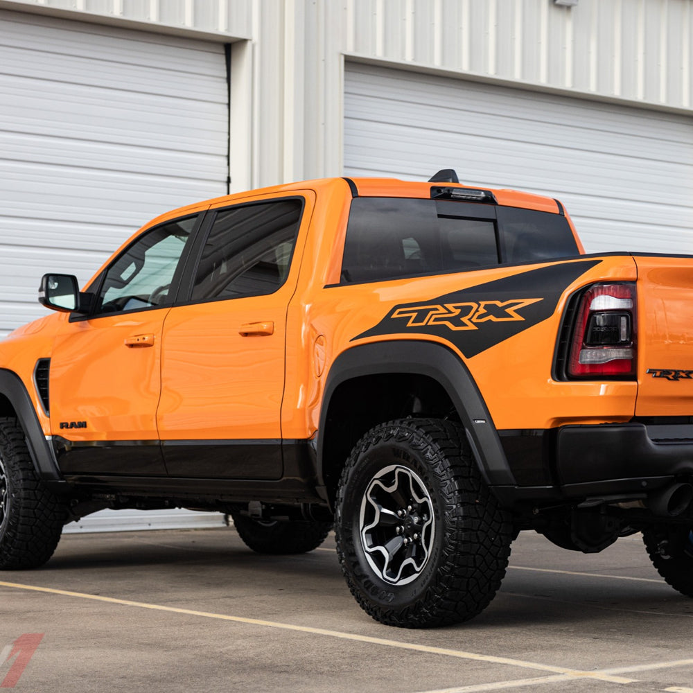 Drivers side view of an orange RAM TRX with matte black factory OEM ignition edition decals.